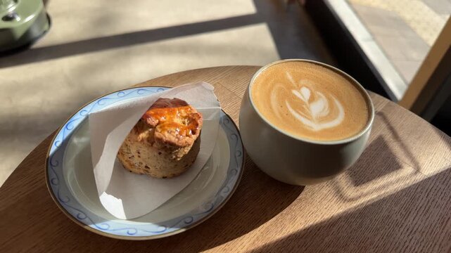 Freshly baked scone and a cup of cappuccino with latte art on a wooden table in a Japan coffee shop