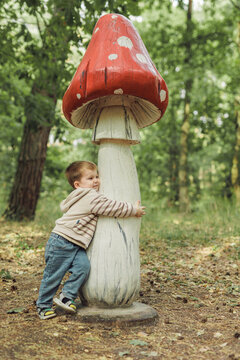 Cute little boy profile view hugging giant wooden mushroom in forest