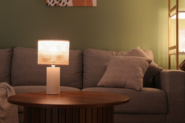 Obraz premium Glowing lamp on coffee table in dark living room at evening, closeup