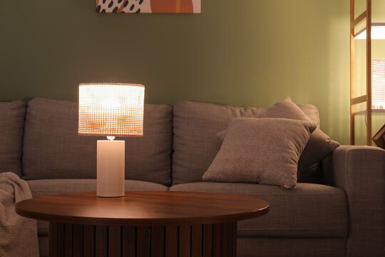 Glowing lamp on coffee table in dark living room at evening, closeup