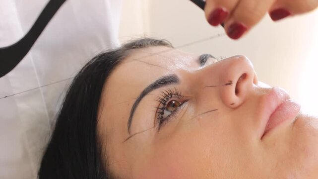 An expert woman is shaping a customer's eyebrows with an archwire and thread in preparation for a hair removal session at a beauty salon in Neiva, Huila, Colombia. Concept of personal care
