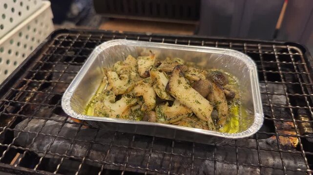 Fresh abalone with herbs and oil grilling in a foil tray on a traditional Japanese charcoal grill