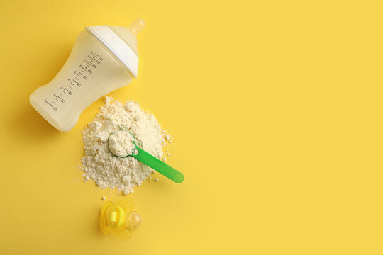 Scoop of powdered baby milk formula with bottle and pacifier on yellow background