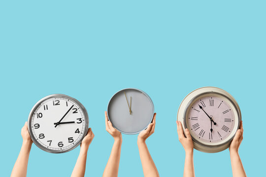 Female hands holding different wall clocks on blue background