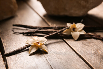 Fototapeta premium Dried vanilla sticks and flowers on wooden background, closeup