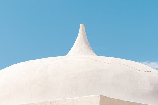 Close up architectural shot of a clean white plastered dome building with a pointed spire against a clear blue sky. Stock photo