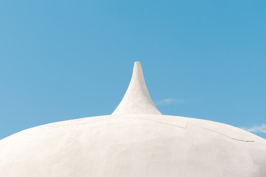 Close up architectural shot of a clean white plastered dome building with a pointed spire against a clear blue sky. Stock photo