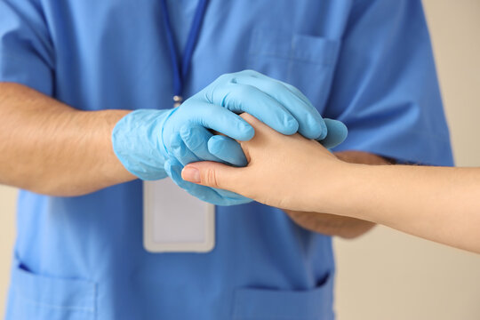 Medical professional in blue scrubs and gloves holding a patients hand, offering comfort and support in a healthcare setting