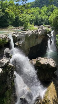 powerful streams of clear water cascade around large weathered rocks in a lush forest gorge, forming a scenic waterfall, splashing rapids and a fresh mountain river landscape