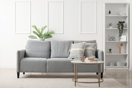 Interior of light living room with grey sofa, table and shelf unit