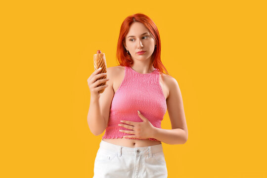 Beautiful young woman with tasty french hot dog on yellow background