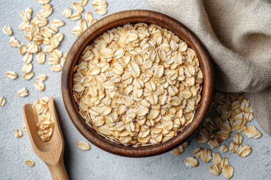 overhead view of a wooden bowl filled with rolled oats, scattered flakes, wooden scoop and beige linen cloth conveying a cozy wholesome breakfast mood