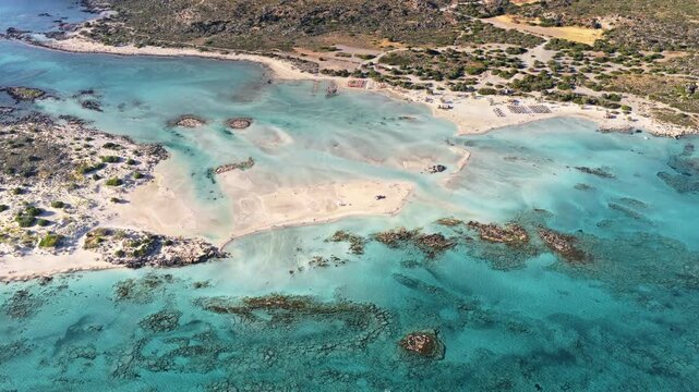 Aerial drone view of a turquoise lagoon with sandbars and straw umbrellas along the beach, Elafonissi, Greece