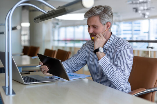 Smiling busy young employee, young entrepreneur using tablet computer, happy businessman executive looking at tab device analyzing finance trading market data working sitting at office desk.