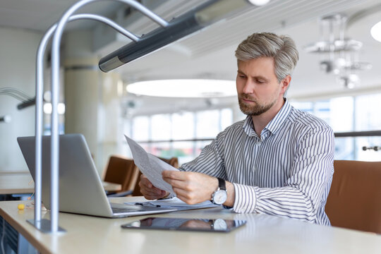 Young businessman sitting at a table at modern office working on a computer and reading report