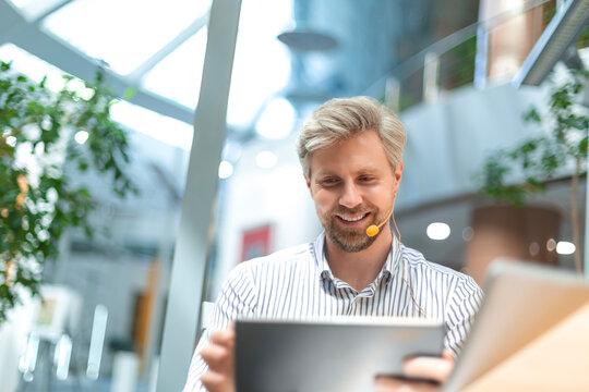 Portrait of successful businessman office worker looking camera holding tablet computer in hands, online customer service, wearing headset for video call, satisfied with work