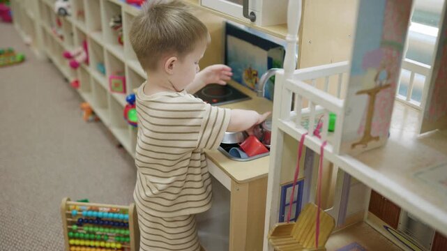 Focused toddler child washing dishes at kids club play kitchen