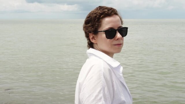 woman after cancer treatment relaxing at the seaside in sunglasses and white linen, representing restorative travel, sun protection and emotional wellbeing