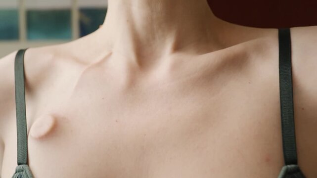close-up of fingers gently touching an implanted chest port near a clothing strap, showing sensitive skin, body awareness and self care during cancer treatment at home