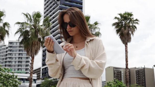 female teenager looks at a smartphone between errands in a city square, representing location services, online communication and independent urban mobility while managing a busy day outdoors