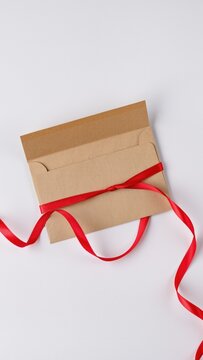 Kraft paper envelope tied with wavy red satin ribbon on white background mockup