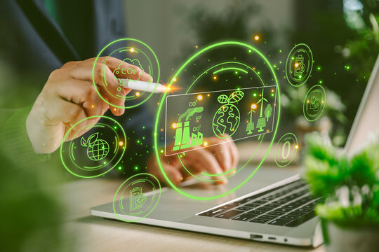 Business hand using stylus on laptop with green holographic CO2 dashboard, climate data, renewable energy icons, carbon reduction, sustainability technology and eco innovation concept.