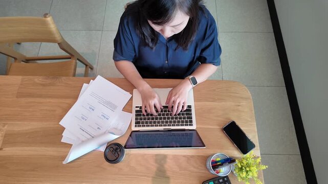 A business professional works on a laptop at a tidy desk while reviewing printed documents in a comfortable office.