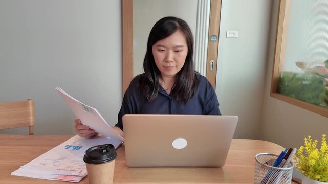 A business professional works on a laptop at a tidy desk while reviewing printed documents in a comfortable office.