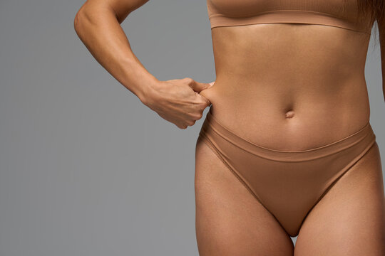 Fit woman in beige underwear gently pinching skin on waist showing real body