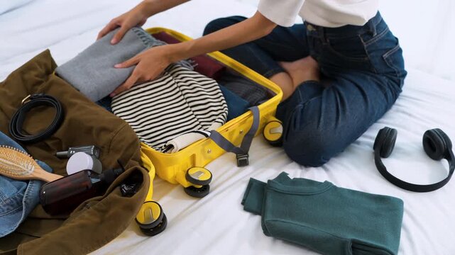 Side view of an Asian woman neatly organizing garments inside an open luggage at home. Concept of travel readiness, minimalist journey and holiday preparation.