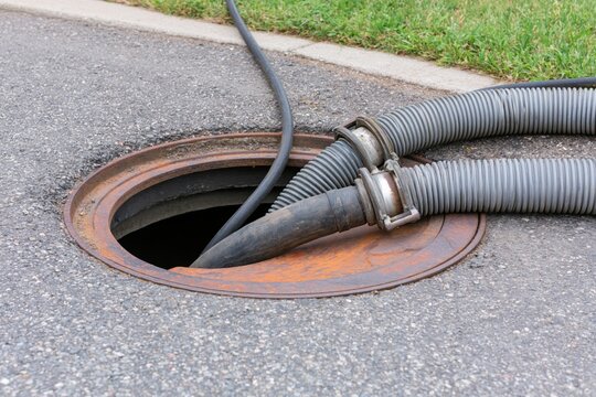 The manhole opening with heavy industrial hoses for sewer cleaning operation
