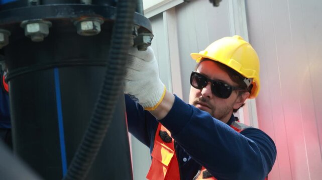 Male technician inspects the coolant inlet and outlet pipes of the cooling tower checks the flange connections and reports to the engine room while testing the cooling system.
