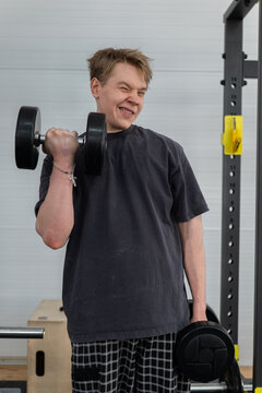 Young man lifting dumbbell during focused strength workout in indoor gym, standing beside power rack and wooden plyo box with neutral wall background and soft studio lighting