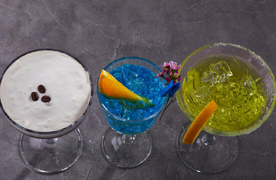 Three cocktails Espresso martini, Blue curacao and Thea standing in a row on a gray background. View from above.