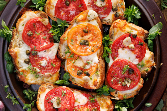 Bruschettas with mozzarella and grana padano cheese, tomatoes, capers and garlic seasoned with aromatic herbs on a plate, top view, close-up view