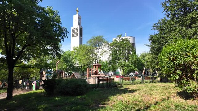 Prague, Czech Republic - May 05, 2026 - Svatopluk Cech Square. Modern church tower and playground on a sunny day with lush green trees