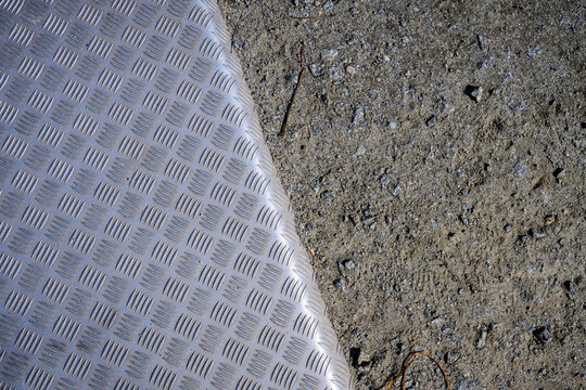 Industrial aluminum tread plate meeting rough gravel ground texture.
