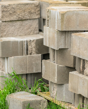 Stacked concrete paving blocks stored outdoors in grass.