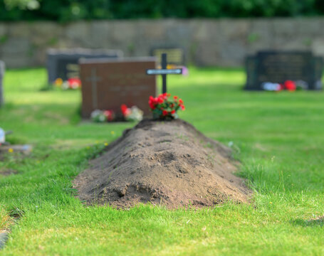Fresh grave mound with flowers and cross in cemetery.
