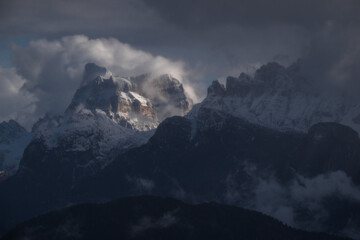 Dramatic landscape of snow-covered mountain peaks emerging through dark winter clouds. Ideal for travel and adventure themes. © marcodenaro