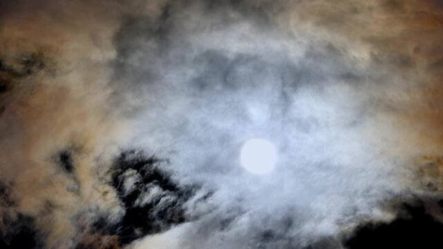 Dramatic clouds slowly drift across the sky, obscuring a bright light source in a dynamic daytime environment for a compelling background.