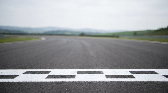 Close-up of a checkered finish line painted on an empty asphalt racing circuit with blurred hills background