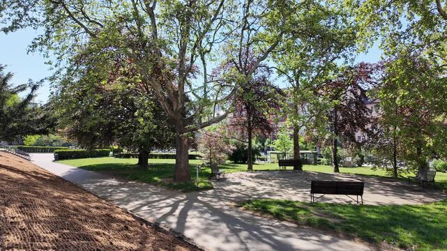 Prague, Czech Republic - May 05, 2026 - Svatopluk Cech Square. Sunny park pathway with benches and lush green trees on a bright day