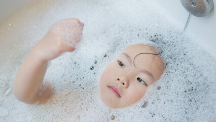 Fototapeta premium A curious young child unwinds in a bathtub full of bubbles, immersed in a peaceful sensory experience as part of a calming daily bathtime routine at home.