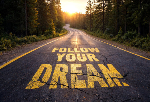 Inspirational road with follow your dream text leading into a scenic forest at sunset