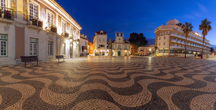 Evening view of Pra a 5 de Outubro in Cascais, Portugal, featuring traditional Portuguese wave pavement, the Town Hall, and the Church of Our Lady of the Navigators.