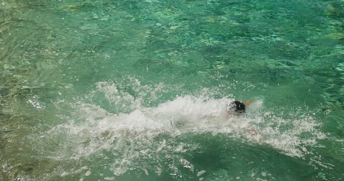 Young Man With Swimming Goggles Dives Headfirst into the Crystal Clear Turquoise Ocean Water on a Beautiful Summer Day for a Refreshing Swim
