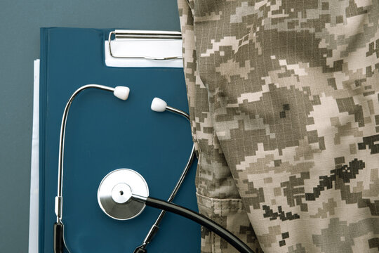 Stethoscope placed on medical clipboard beside digital camouflage uniform, representing military healthcare, veteran support and field medicine.