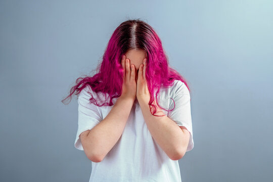 Teen girl with pink hair hiding her face in shame or despair, concept of mental health, stress, anxiety, trauma, loneliness and need for psychological support in studio.