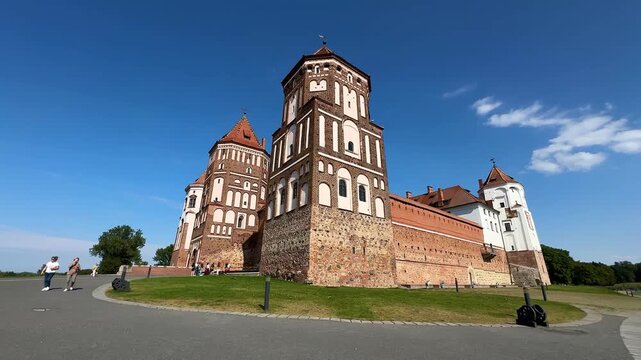 Mir Castle, Belarus. Historic castle showcases unique architectural features with visitors strolling along the pathway, surrounded by lush greenery and a clear blue sky